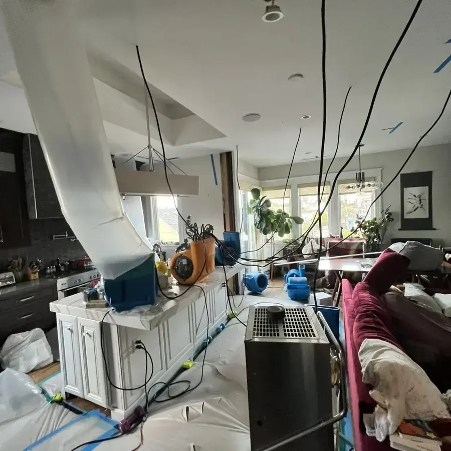 Drying ducts and air movers set through an open kitchen and living area after a leak