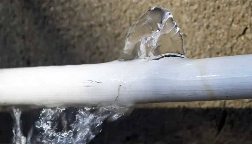 Water spraying hard out of a split plastic water supply pipe