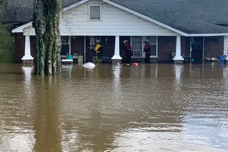 Brown floodwater spread across a living room, around a small table and storage bins
