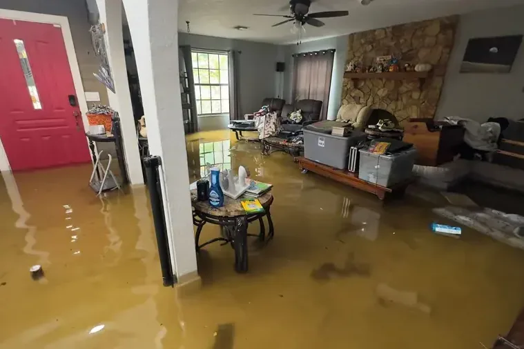 Brown floodwater pooled across a living room near a red front door and storage bins