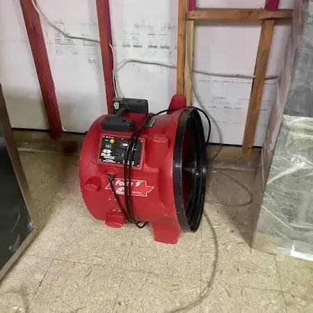 A red air mover standing against an opened wall with exposed studs and insulation behind it