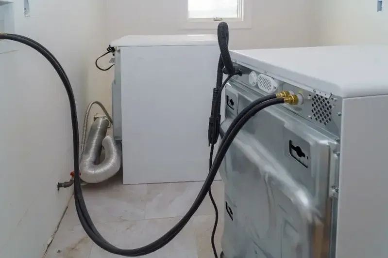 Washing machine pulled away from the wall with its hoses showing