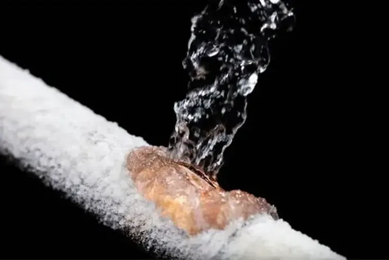Split copper pipe coated in ice and spraying water