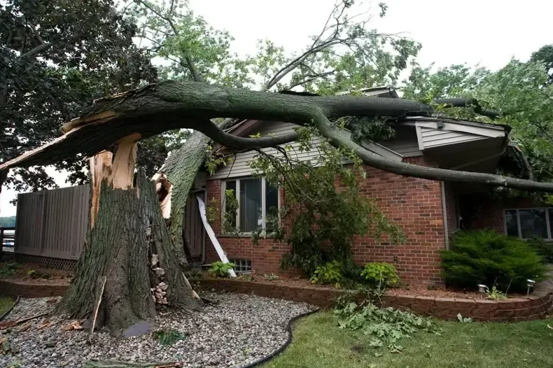 Tree trunk split across the roof of a brick ranch house after a thunderstorm